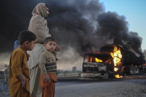 Boys stand next to a man as they watch fuel trucks which were set ablaze in the Bolan district of Pakistan's Baluchistan province